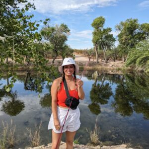 Young woman smiling in front of a lake while holding a fishing pole