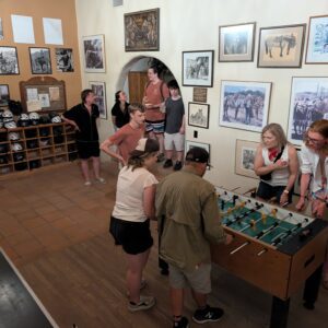 Four people playing foosball in a large room while other people watch