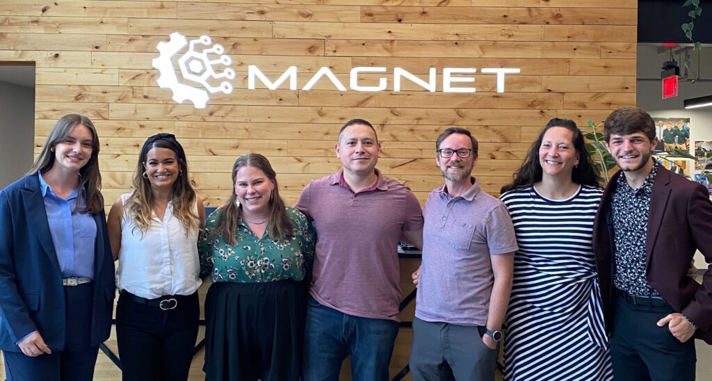 Michelle Clever, Melanie Muscolo, Kaylyn Bass, Anjelo Pina, Torrey Babson, Laura Larson, and Brady Anashansel in front of a sign that says MAGNET.